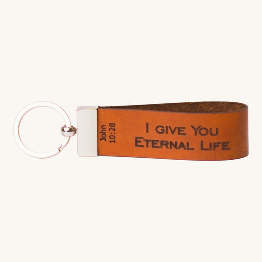 Holy Matters vegetable-tanned leather keychain engraved with John 10:28 scripture on a brown strap with metal ring